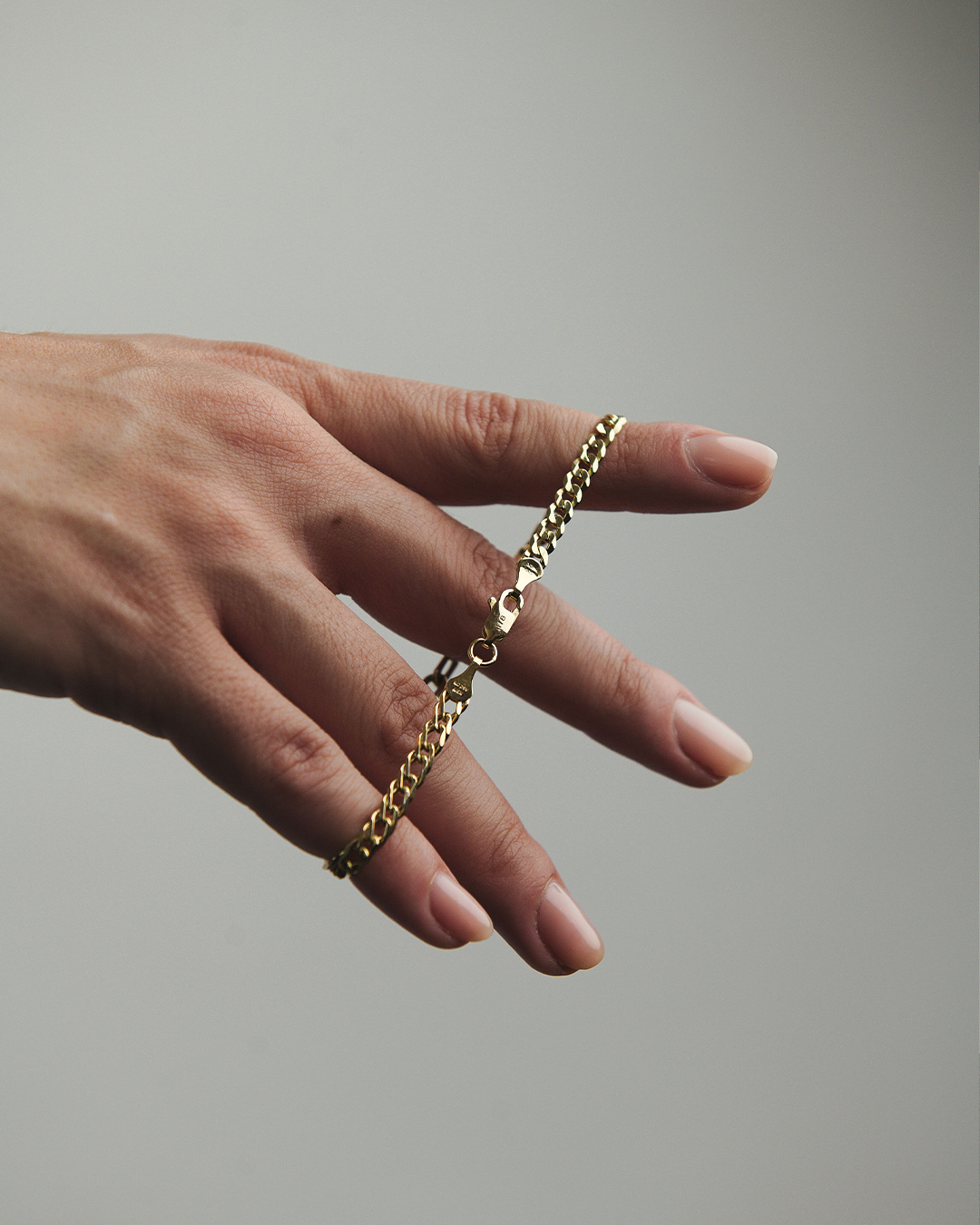 Primer plano de una mano de modelo sosteniendo una pulsera combinada de oro amarillo de 10 quilates, con diseño de eslabones tipo cubano y paperclip, destacando su acabado pulido y el broche de seguridad grabado con la marca M18.
