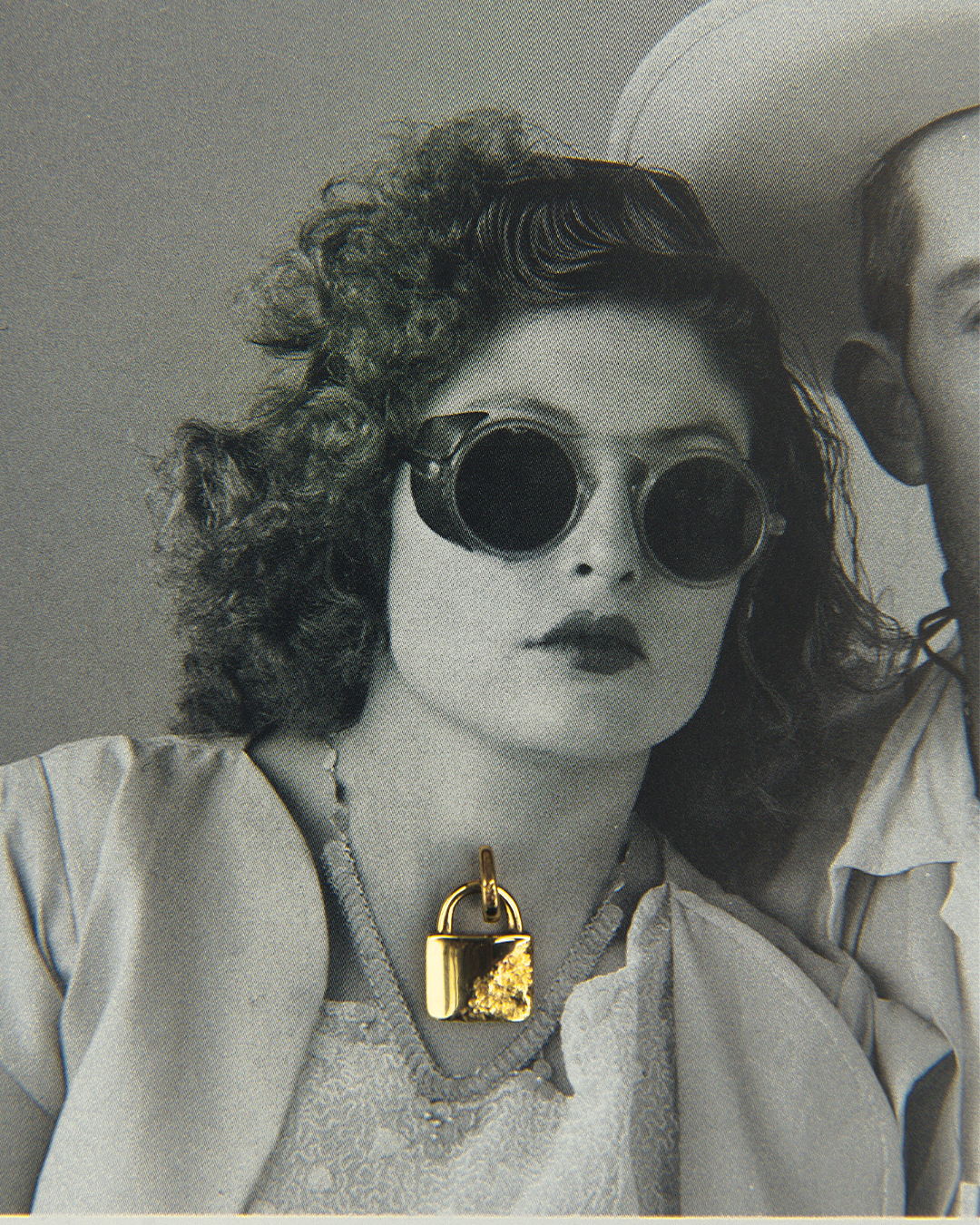 Fotografía vintage en blanco y negro de una modelo con gafas de sol usando un dije de oro amarillo de 10 quilates con forma  de candado de M18, destacando el colgante como punto focal.