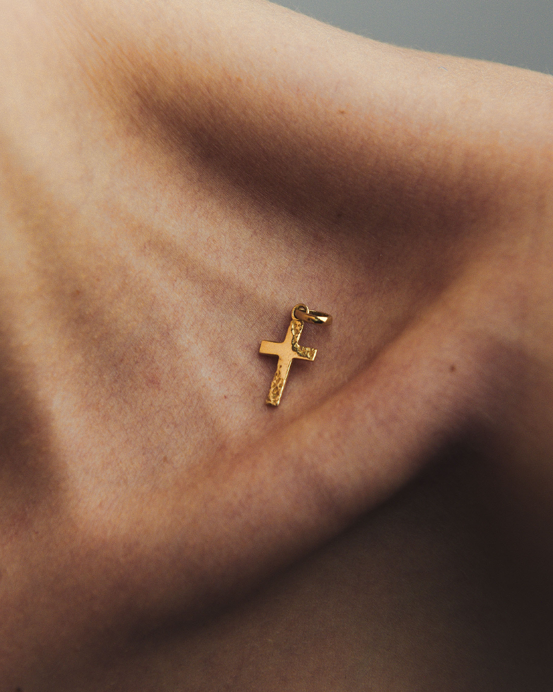 Detalle del frente de un dije en forma de cruz de oro amarillo de 10 quilates de M18 sobre la clavícula de una modelo.