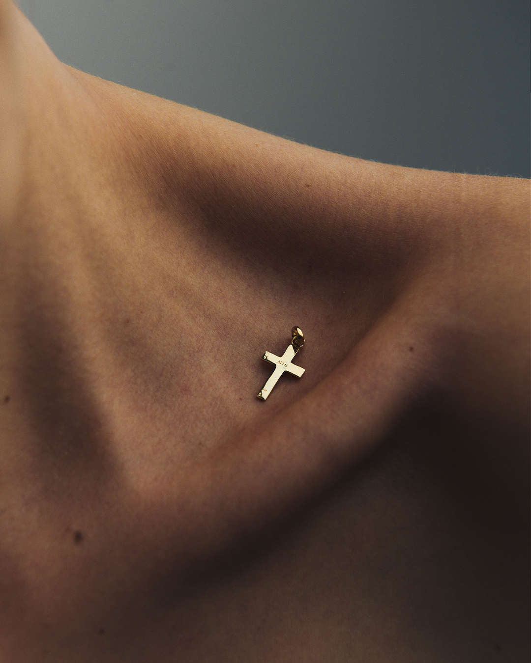 Detalle de un dije en forma de cruz de oro amarillo de 10 quilates de M18 sobre la clavícula de una modelo.