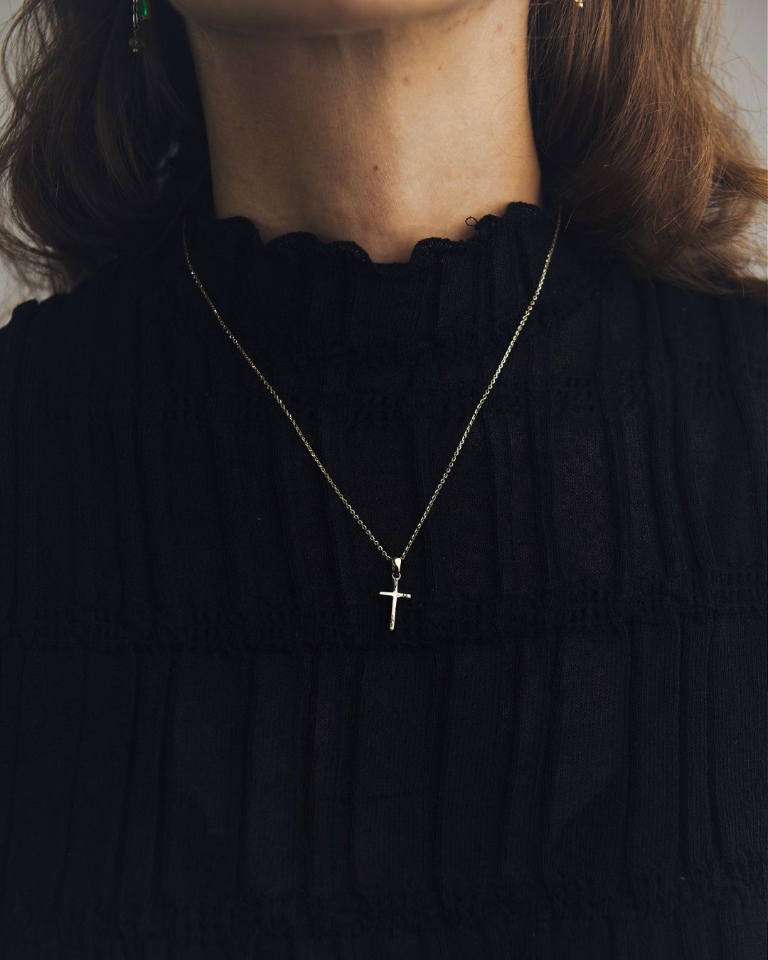 Modelo mujer luciendo un dije de cruz en oro blanco de 10 quilates con cadena de M18 sobre blusa negra.