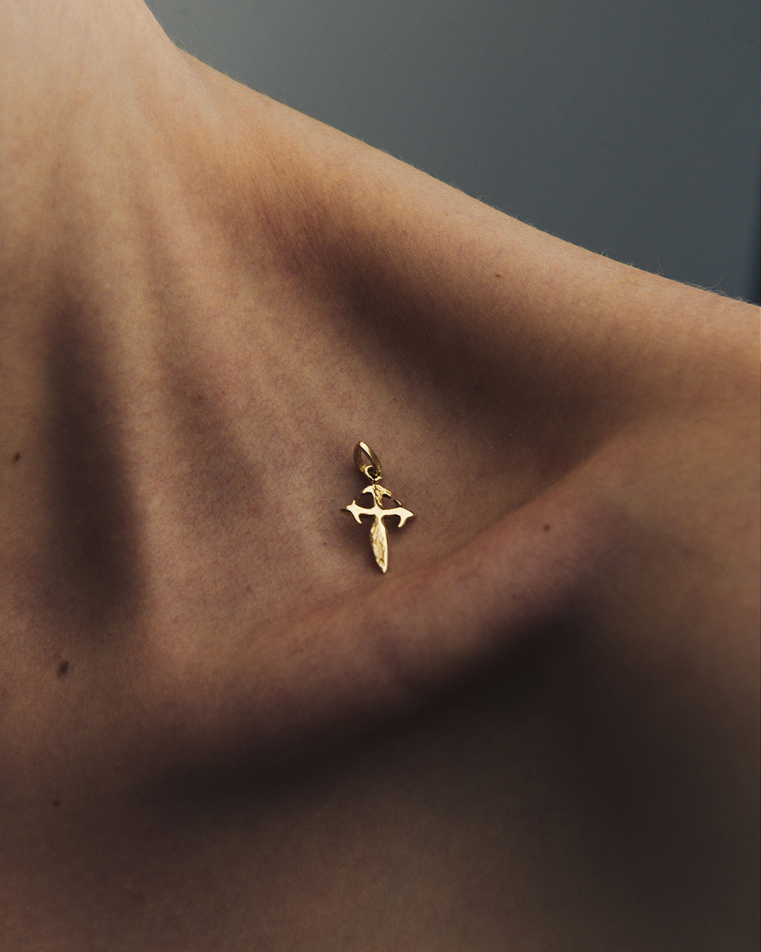 Detalle de la clavícula de una modelo sosteniendo un dije en forma de cruz medieval de oro amarillo de 10 quilates de M18.