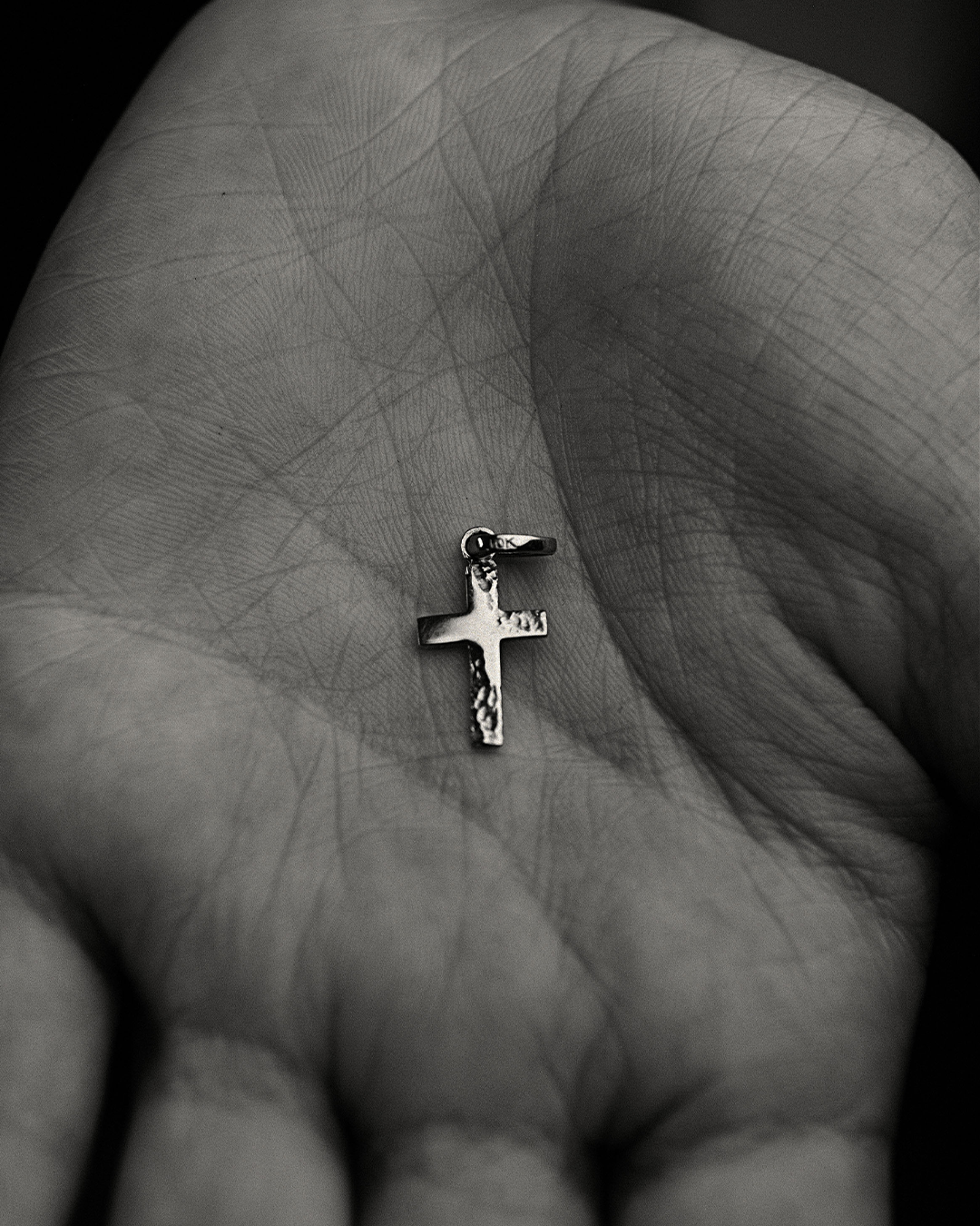 Fotografía en blanco y negro de un dije en forma de cruz de oro amarillo de 10 quilates de M18 sobre la palma de la mano de una modelo.