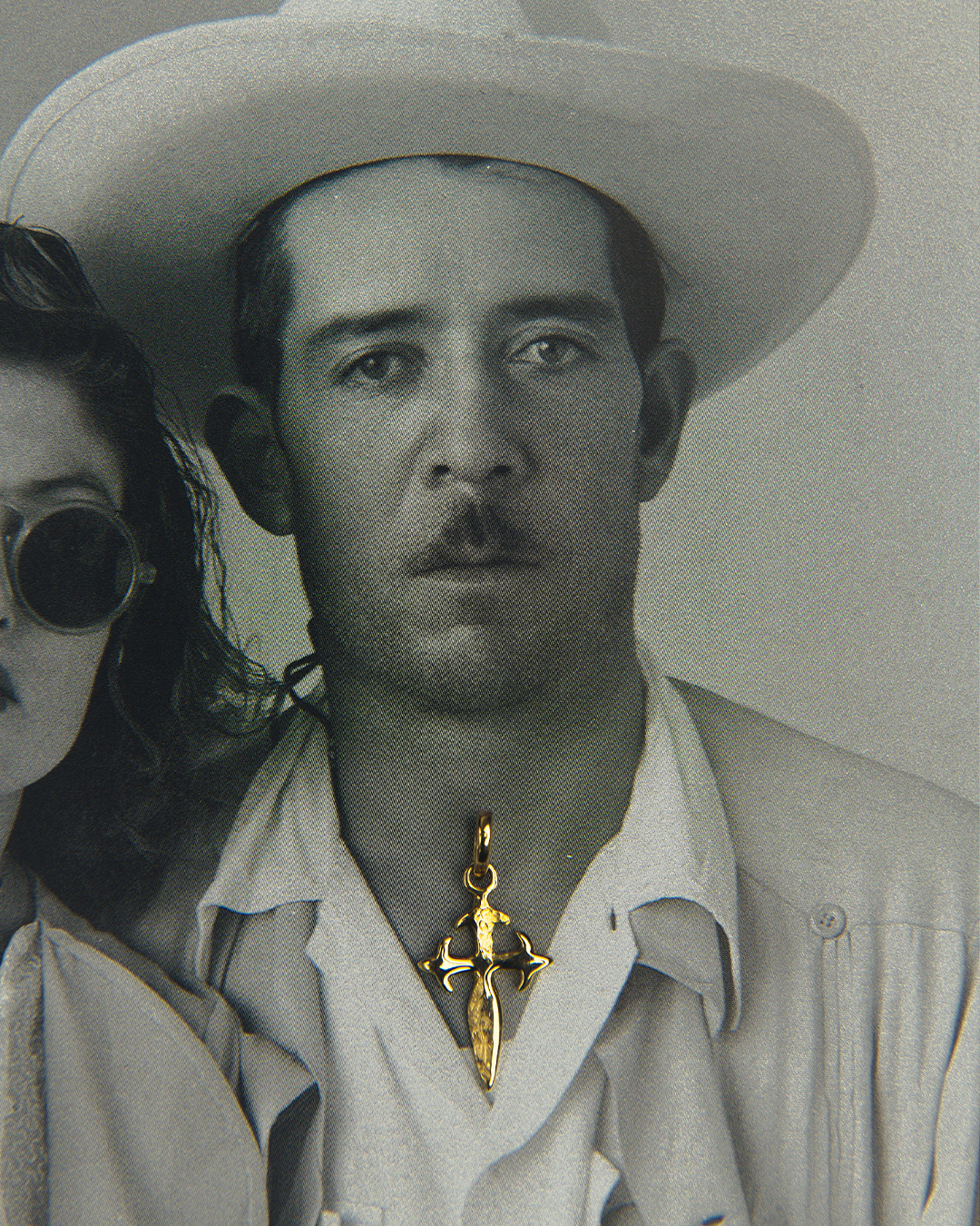 Fotografía vintage en blanco y negro de un modelo fingiendo usar un dije de oro amarillo de 10 quilates con dije en forma de cruz medieval de M18, destacando el dije como punto focal.