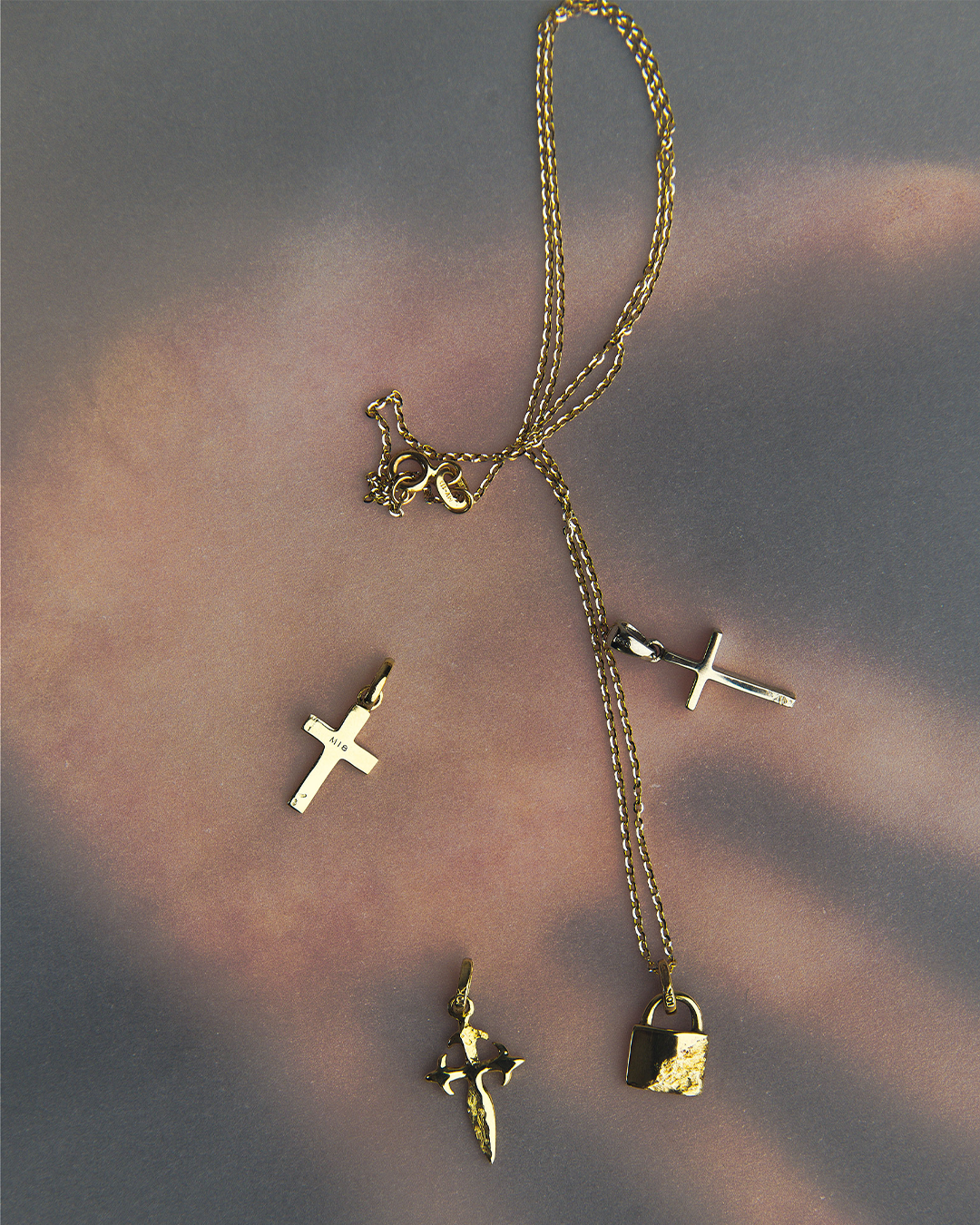 Cadena y colección de dijes de oro de 10 quilates de M18, incluyendo cruces y un candado, sobre fondo transparente.