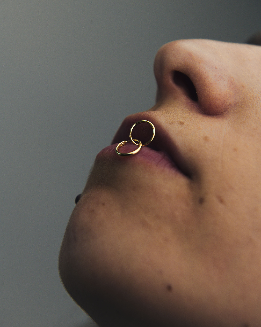 Modelo vista de perfil sosteniendo mini hoops de oro amarillo de 10 quilates de M18 sobre los labios.